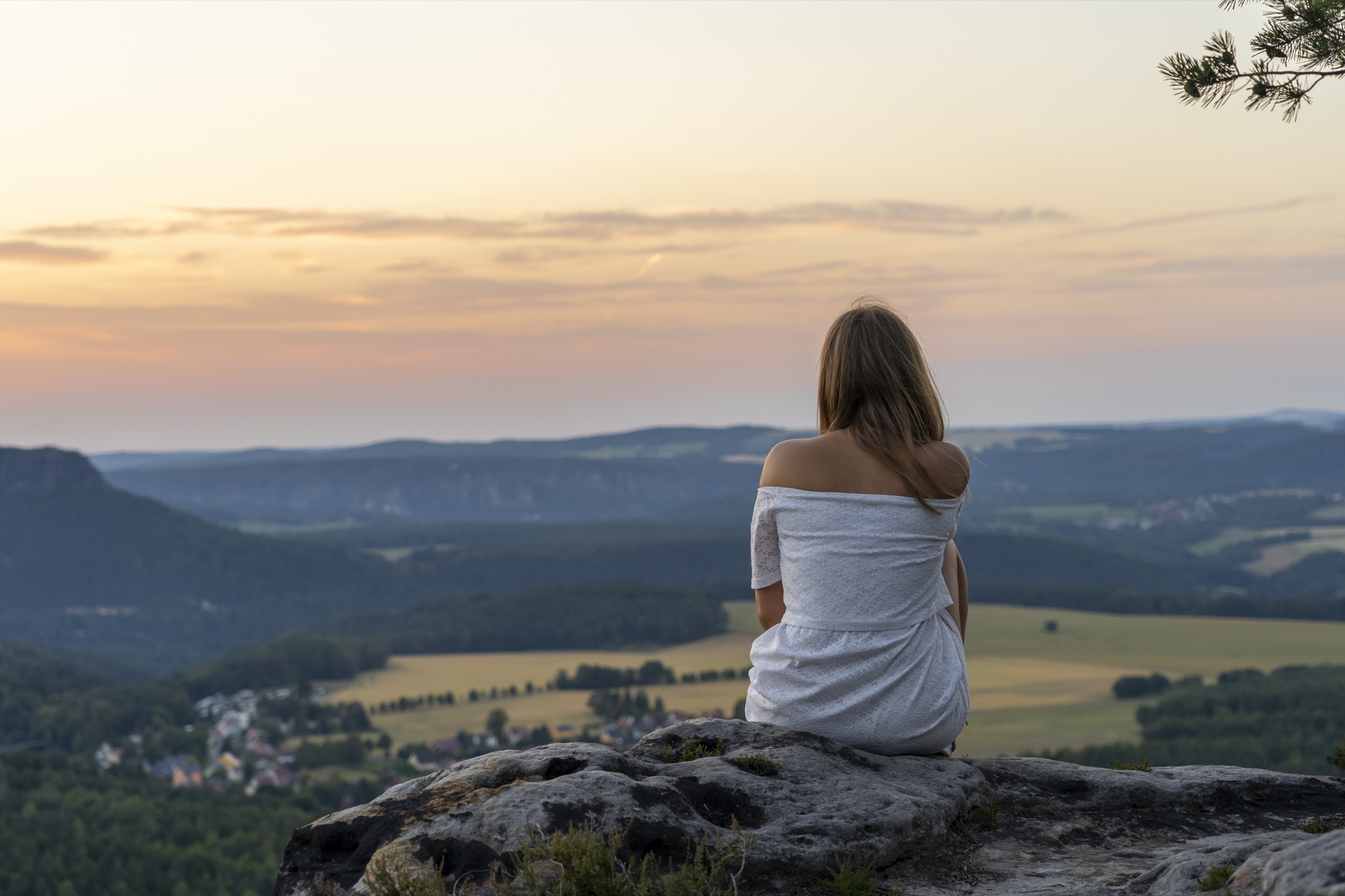 Frau sitzt auf einem Felsen und blickt ruhig ins Tal