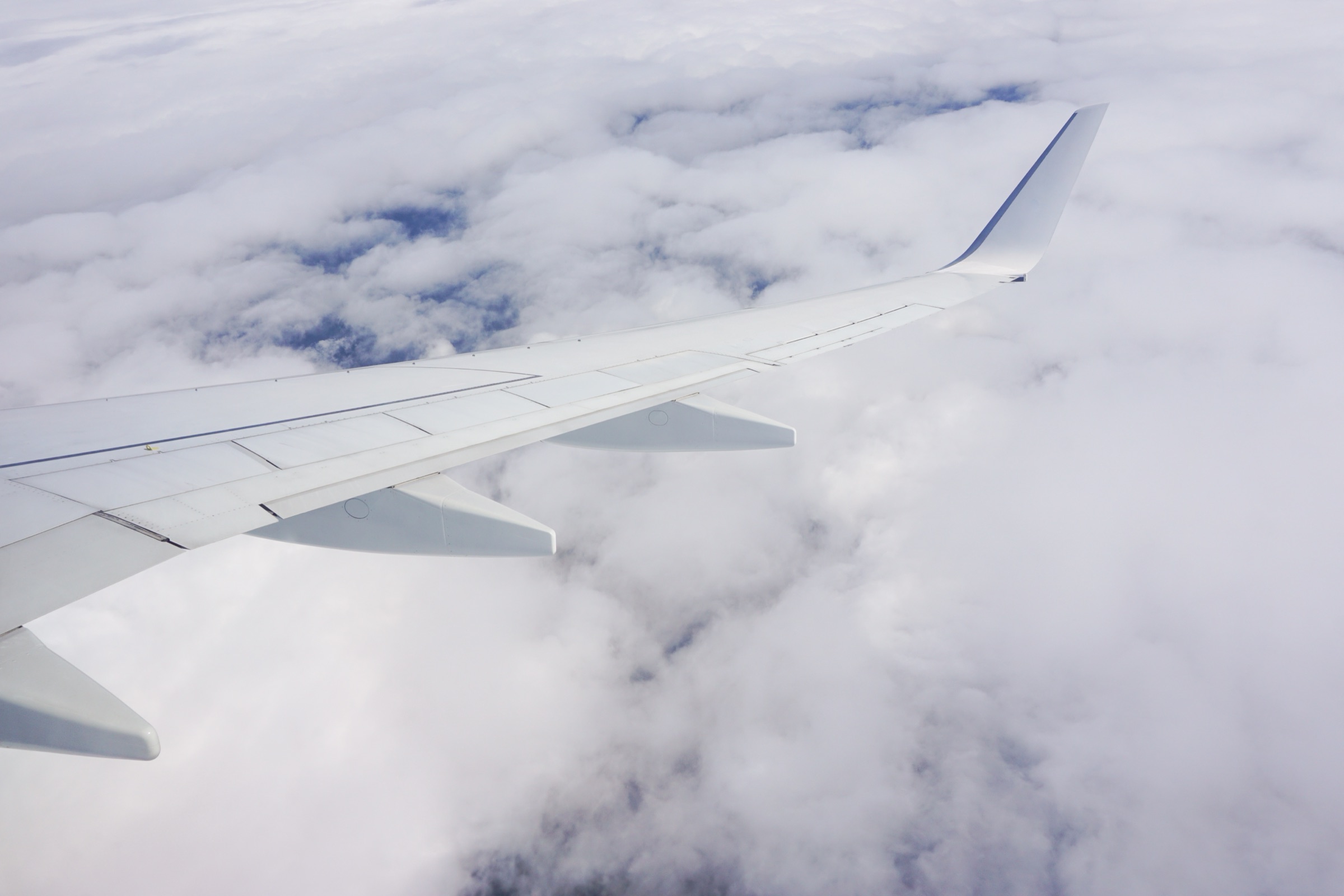 Blick aus dem Flugzeugfenster auf die Tragfläche über den Wolken